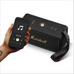 Marshall – Middleton II - Altavoz Portátil - Black & Brass, altavoz negro apoyado sobre una superficie blanca, con un teléfono