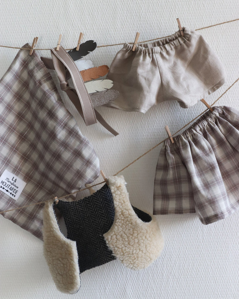 Tenue pour poupée Philéas - tenue garçon composée d'un short en lin beige, d'une blouse en voile de coton à carreaux avec un fil en lurex argent, un gilet de berger réversible - un coté fausse fourrure mouton et un côté lainage chevrons ainsi que d'une coiffe d'indien avec des plumes de cuir - Collection automne/hiver 2020 La manufacture moutarde à retrouver sur amaetc.com, concept store eco friendly pour bébés, enfants et toute la famille