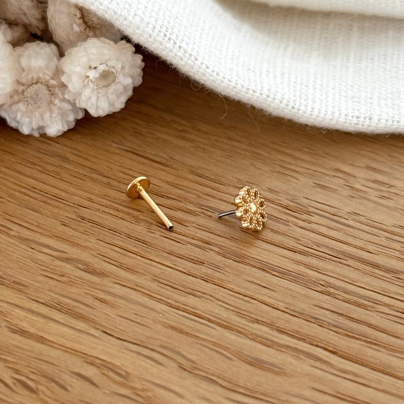Instants Plaisirs – Piercing Oreille "Apie" Plaqué Or, un piercing doré en forme de fleur sur une surface en bois