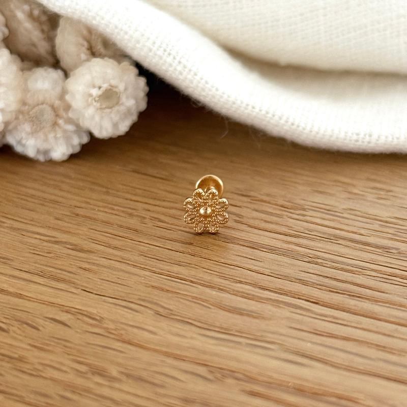 Instants Plaisirs – Piercing Oreille "Apie" Plaqué Or, petit piercing doré en forme de fleur sur une table en bois