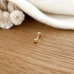 Instants Plaisirs – Piercing Oreille "Neo" Plaqué Or, un piercing doré en forme de fleur posé sur une table en bois