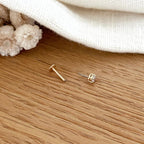 Instants Plaisirs – Piercing Oreille "Dani" Plaqué Or, un piercing doré avec un petit diamant, posé sur une table en bois