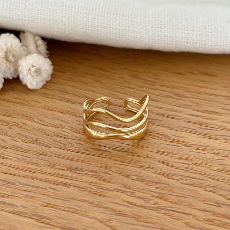 Instants Plaisirs – Bague "Mila" Acier, bague dorée à trois anneaux ondulés posée sur une table en bois