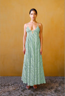 Woman in light green patterned maxi dress with thin straps, standing against mustard wall