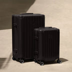 Set of two black GYL Intemporelle rigid suitcases, cabin and hold sizes, placed on concrete floor. #black_color