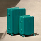 Set of two GYL Intemporelle water green rigid suitcases, cabin and hold sizes, placed on concrete floor. #color_green