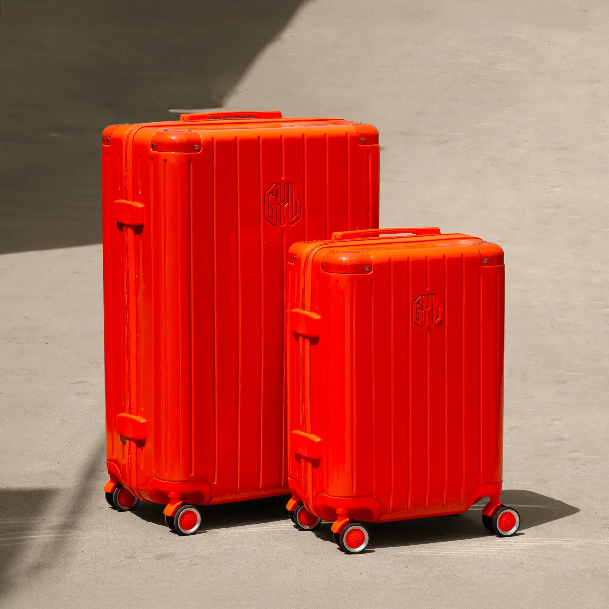 Set of two GYL Intemporelle orange rigid suitcases, cabin and hold sizes, placed on concrete floor. #dark_orange_color