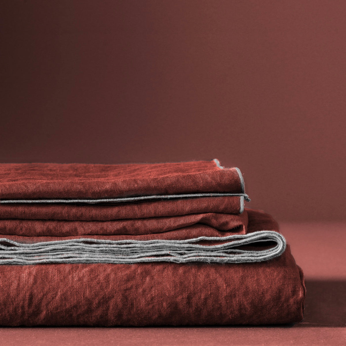 Blanc Cerise – Autour Du Lin - Nappe - Lin - Rouge Terre Bourdon Lin, linge de lit en lin froissé rouge brique, plié sur fond uni
