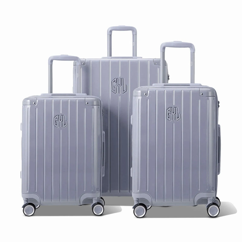 Trois valises rigides GYL Intemporelle argent, format cabine et soute, avec poignée trolley déployée.  #couleur_argent