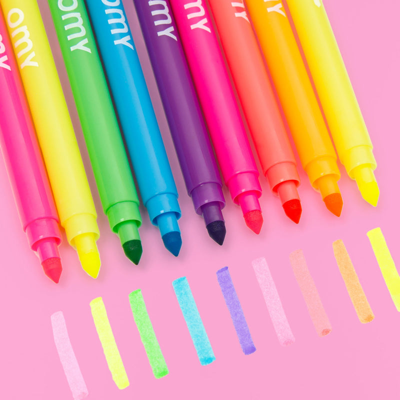 Crayons feutres fluo OMY posés sur table rose – Kit de coloriage DIY 