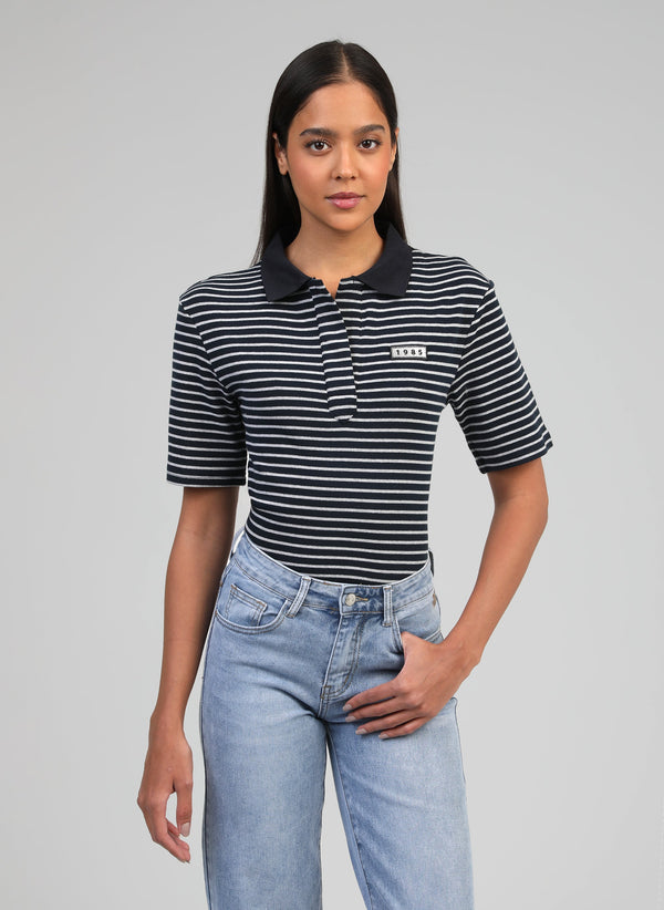 An'ge – Assia Polo Marineblauw, model in een zwart-wit gestreepte polo en een blauwe jeans