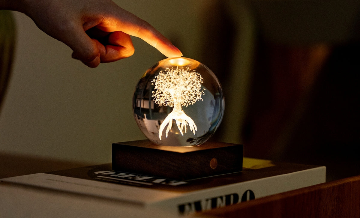 Gingko Design – Lampka Amber Crystal - Drzewo Życia, dłoń dotykająca świecącej szklanej kuli z wygrawerowanym drzewem