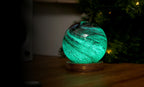Gingko Design – Leuchte Astraglass - Stellar Ocean - 2 Größen, leuchtende grüne kugelförmige Nachttischlampe auf Holzsockel
