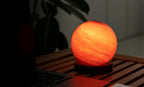 Gingko Design – Lampa Astraglass - Sand Storm - 2 rozmiary, kulista świecąca pomarańczowa lampa stołowa na drewnianym stole