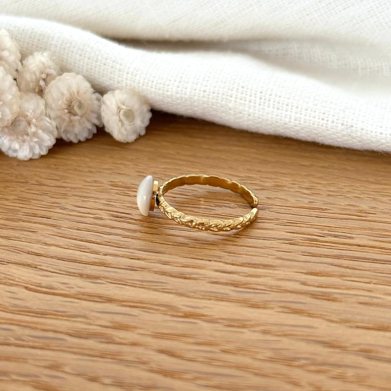 Instants Plaisirs – Bague "Aline" Acier, bague dorée avec une pierre blanche, posée sur du bois