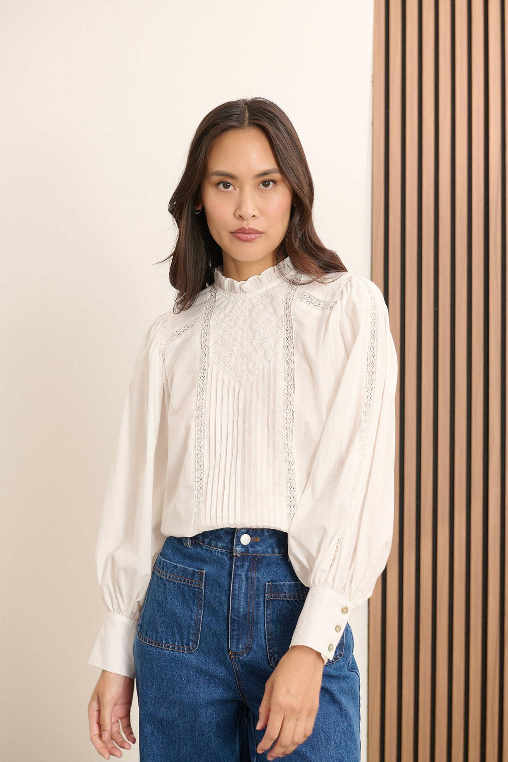 Femme portant la blouse BELLA coloris blanc, une blouse ample en voile de coton avec découpe composée de dentelle et plis.