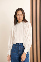 Femme portant la blouse BELLA coloris blanc, une blouse ample en voile de coton avec découpe composée de dentelle et plis.