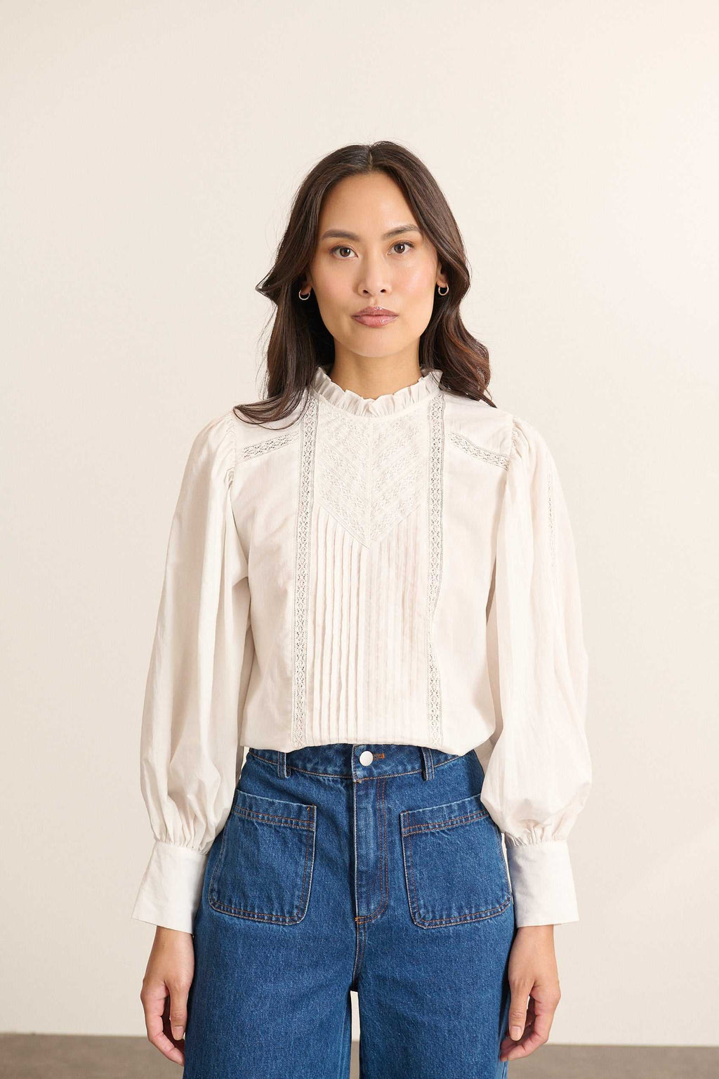Mannequin femme de face portant une blouse ample blanche en voile de coton, col volanté et empiècements en dentelle.