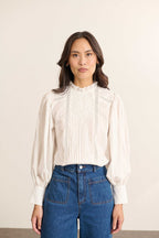 Mannequin femme de face portant une blouse ample blanche en voile de coton, col volanté et empiècements en dentelle.