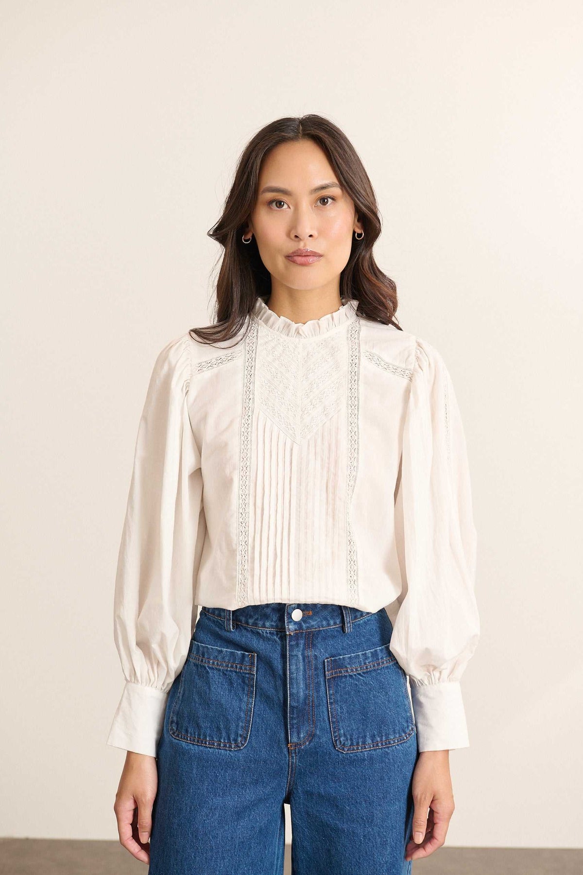 Mannequin femme de face portant une blouse ample blanche en voile de coton, col volanté et empiècements en dentelle.