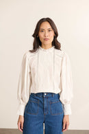 Mannequin femme de face portant une blouse ample blanche en voile de coton, col volanté et empiècements en dentelle.