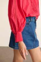 Femme portant la blouse BELLA coloris cerise, une blouse ample en voile de coton avec découpe composée de dentelle et plis.