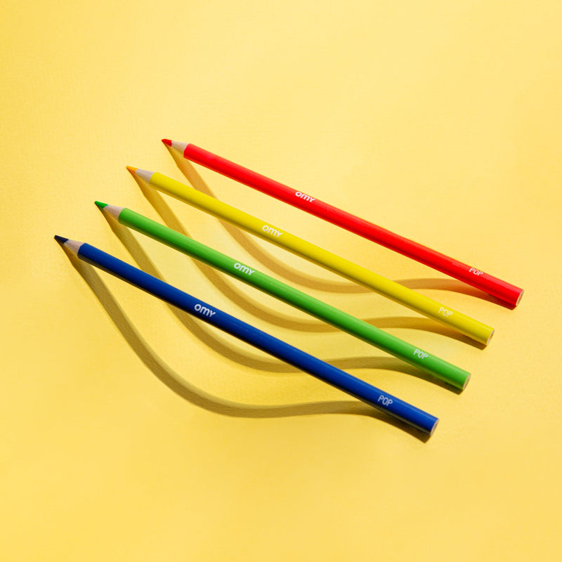 Crayons de couleur OMY étalés sur fond jaune – outils de dessin colorés pour enfants et adultes créatifs.