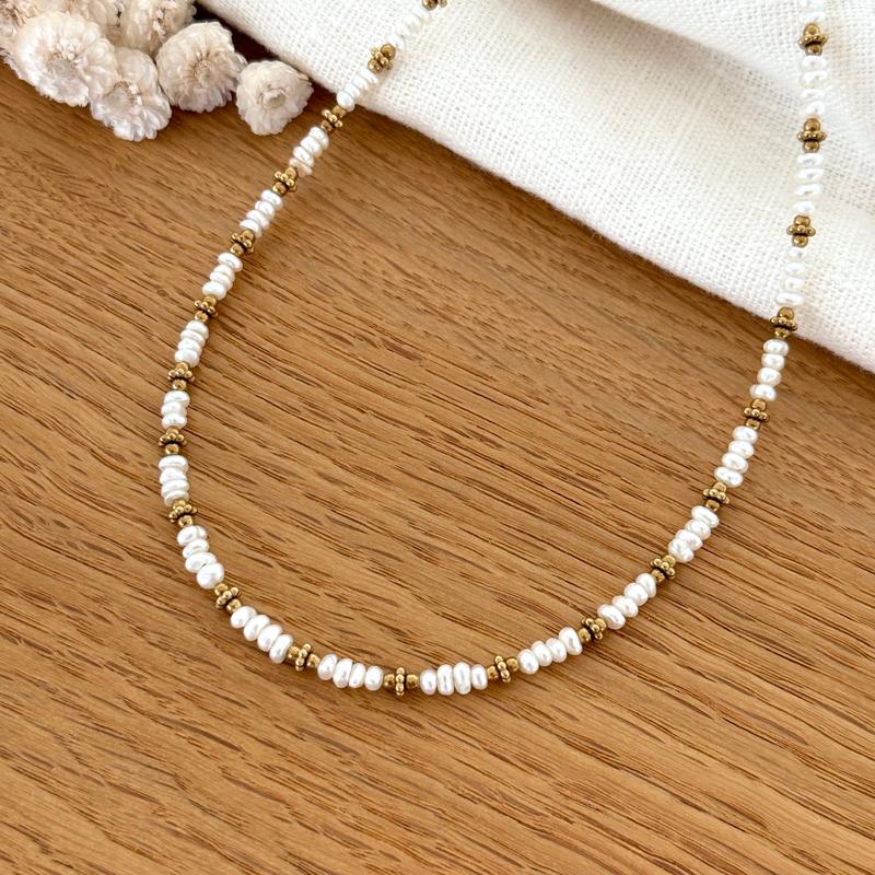 Instants Plaisirs – Collier "Emilie" Acier, collier de perles blanches et de perles dorées sur une table en bois
