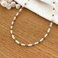 Instants Plaisirs – Collier "Emilie" Acier, collier de perles blanches et de perles dorées sur une table en bois