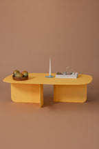 Moderne Couchtisch Livia in Gelb mit Kerze und Dekoration auf braunem Untergrund.