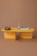 Moderne Couchtisch Livia in Gelb mit Kerze und Dekoration auf braunem Untergrund.