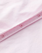 Détail d’un tissu popeline rose clair en coton, lisse et léger, avec une finition soignée comprenant des boutons assortis cousus sur une couture propre.
