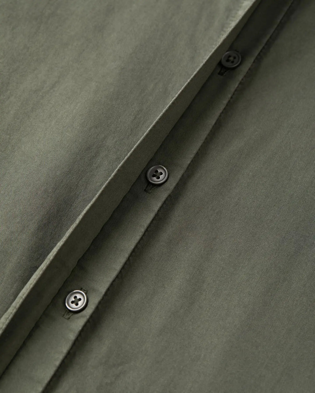 Tissu popeline en coton kaki avec boutonnières noires sobres, montrant la qualité et la finesse de la matière idéale pour un pantalon léger et élégant.
