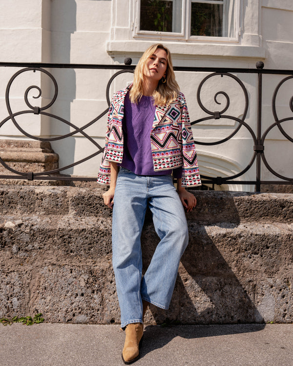 Michonet – Jacka Rombo, blond kvinnlig modell, iklädd färgglad jacka, lila tröja och jeans