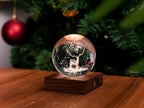 Gingko Design – Bernstein-Kristall-Licht – Hirsch, leuchtende Weihnachtskugel mit einem Hirsch auf einem Holztisch