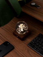 Gingko Design – Amber Crystal-lampa - Cyklist, en lysande glaskula med en cyklist på ett träskrivbord