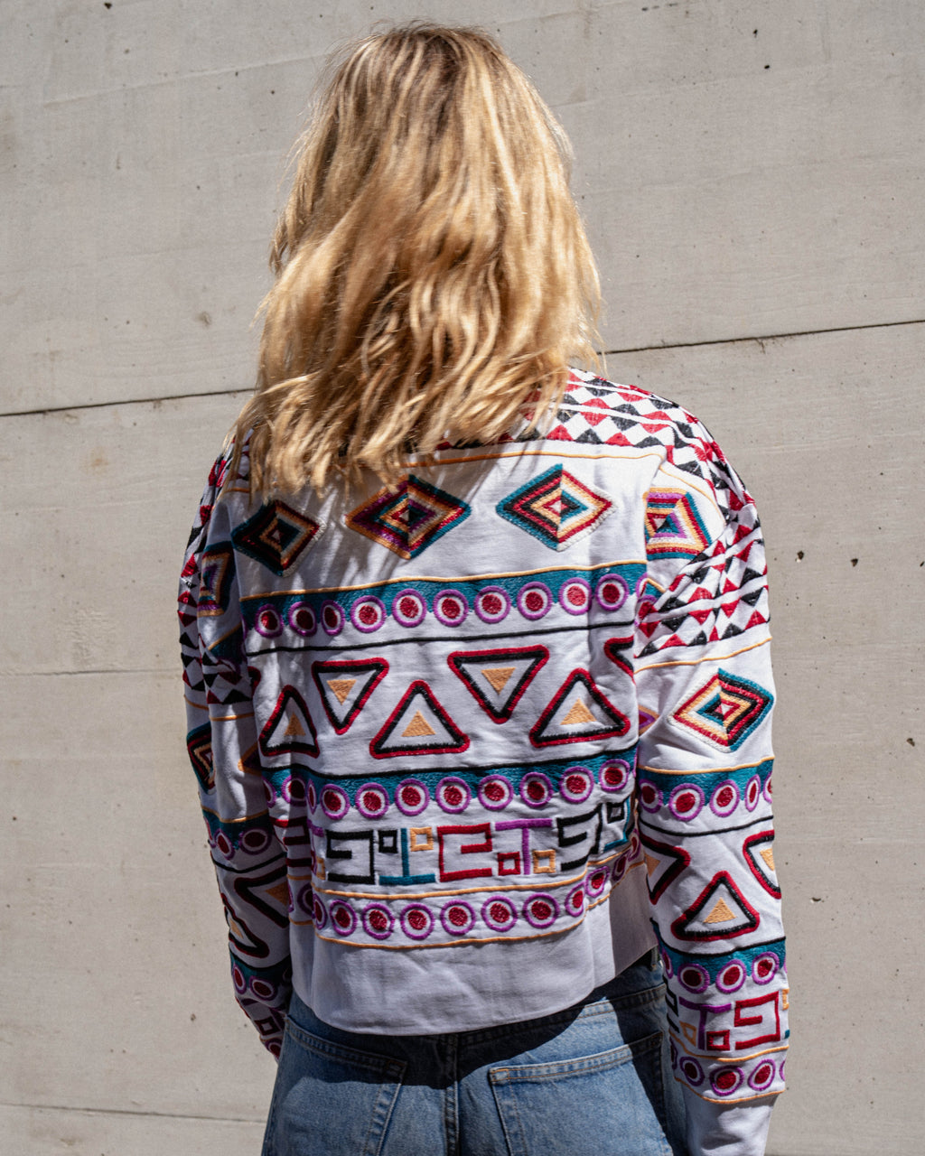 Michonet – Sweat Rombo, femme de dos portant un pull blanc brodé de motifs colorés