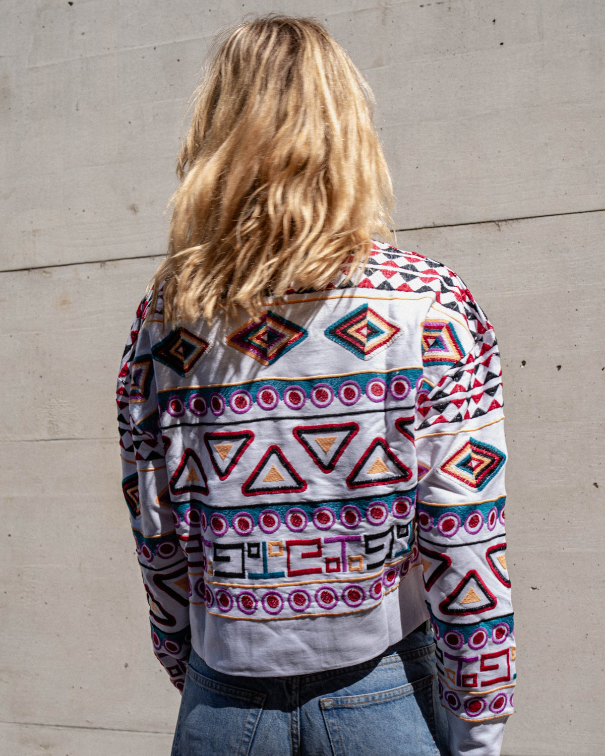Michonet – Sweat Rombo, femme de dos portant un pull blanc brodé de motifs colorés