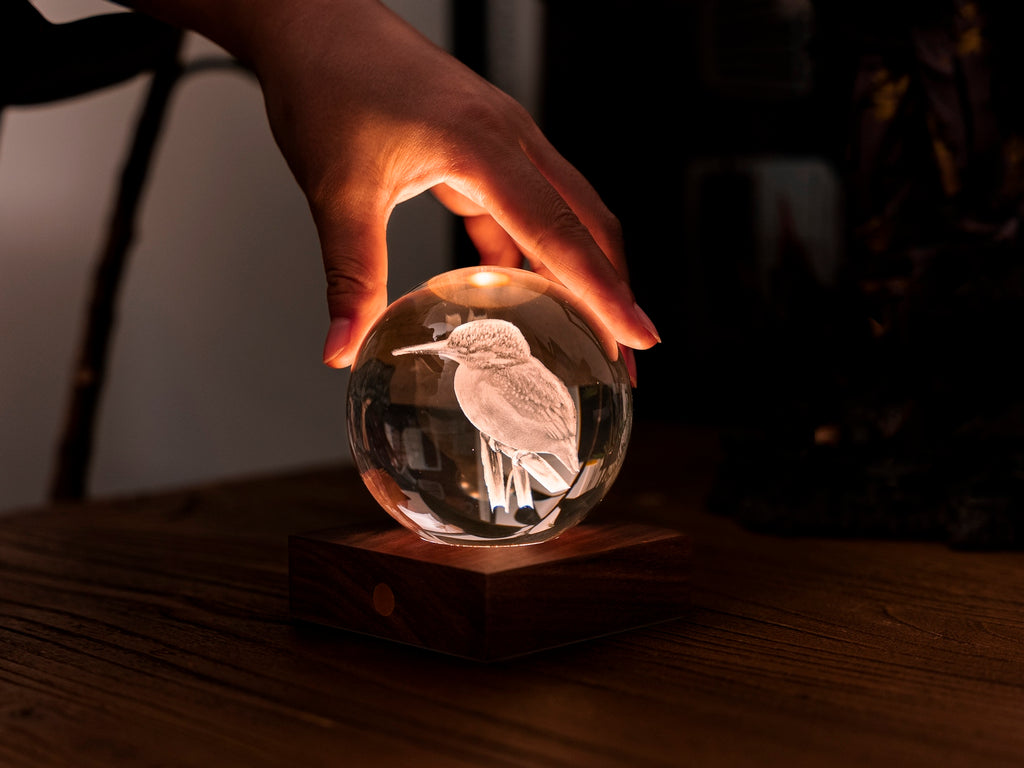 Gingko Design – Amber Crystal-lys - Isfugl, en hånd sætter en lysende krystalkugle på en træsokkel