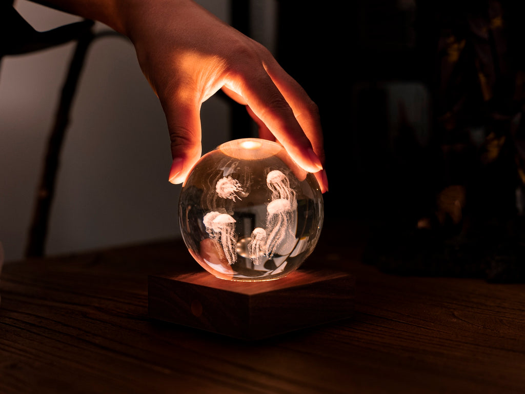 Gingko Design – Lampka Amber Crystal - Meduza, dłoń trzymająca świecącą szklaną kulę z meduzami w środku
