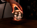 Gingko Design – Lampka Amber Crystal - Meduza, dłoń trzymająca świecącą szklaną kulę z meduzami w środku
