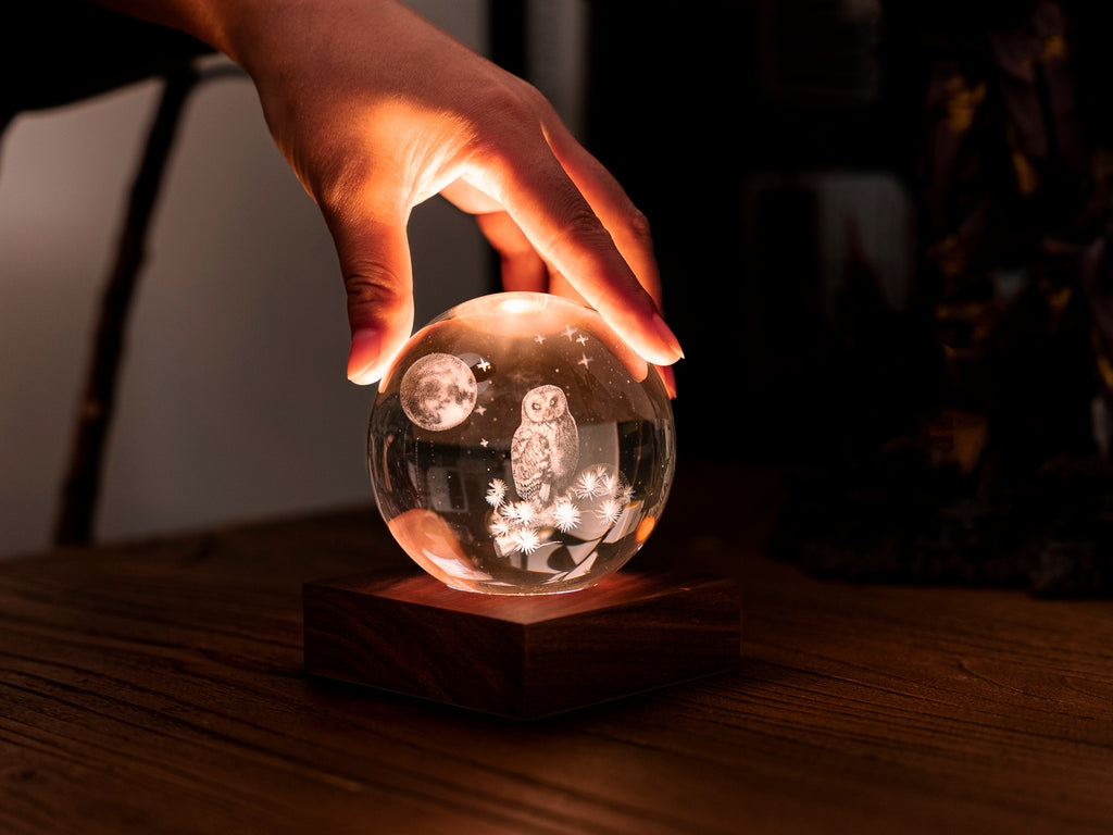 Gingko Design – Amber Crystal-lys - Ugle og Måne, hånd placeret på en lysende krystalkugle med en ugle