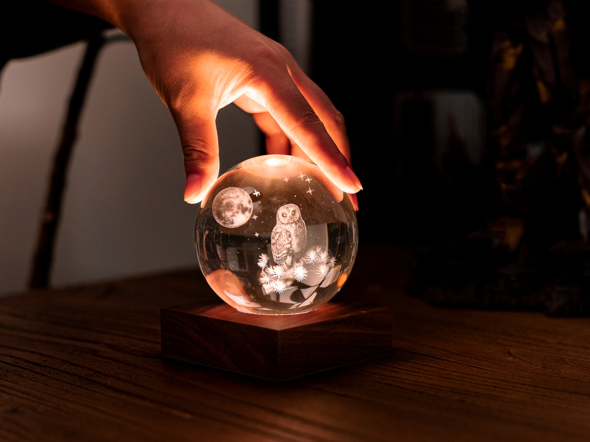 Gingko Design – Amber Crystal-lys - Ugle og Måne, hånd placeret på en lysende krystalkugle med en ugle