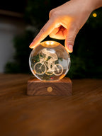 Gingko Design – Amber Crystal-lampa - Cyklist, en hand som rör vid en lysande glaskula med en cyklist