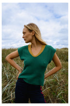 Michonet – Ärmlös Väst Knitted Green, modell i grön tröja och blå byxor, poserande i profil i gräset