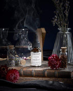 L'Élixir du Marabout de Garancia serum placed on an old grimoire, surrounded by red flowers, apothecary vials and a mystical smoke evoking a witchcraft laboratory.
