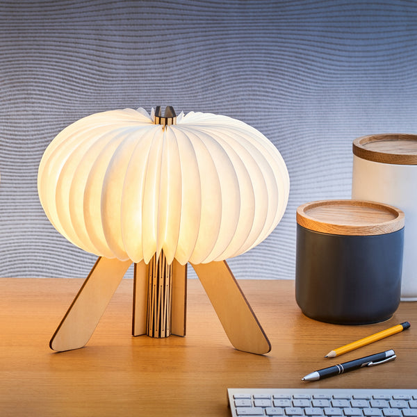 Gingko Design – Lámpara The R-Space - Arce, lámpara de sobremesa de madera clara y pantalla plisada blanca sobre un escritorio