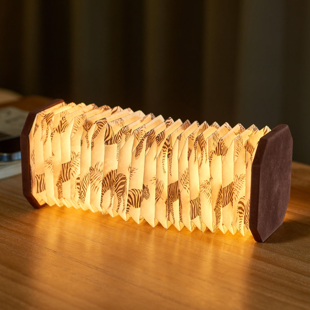 Gingko Design – Lampe Smart Accordion - Velours Marron Zèbre, lampe accordéon lumineuse avec motifs zébrés posée sur une table en bois
