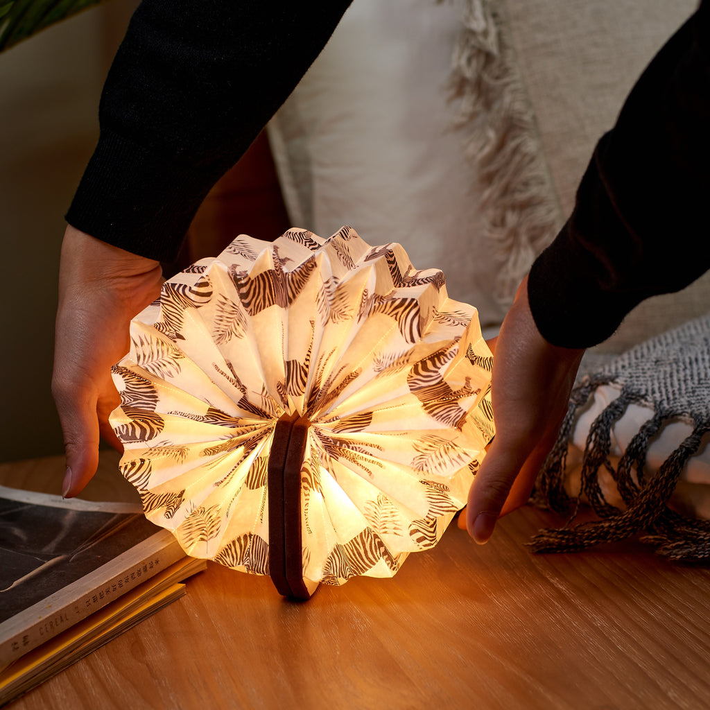 Gingko Design – Lampe Smart Accordion - Velours Marron Zèbre, lampe livre ouverte avec motif zèbre, posée sur une table en bois