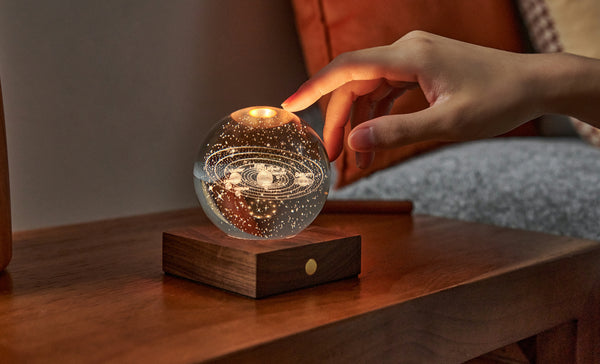 Gingko Design – Luz Amber Crystal - Sistema Solar, una mano toca una lámpara de noche en forma de esfera luminosa
